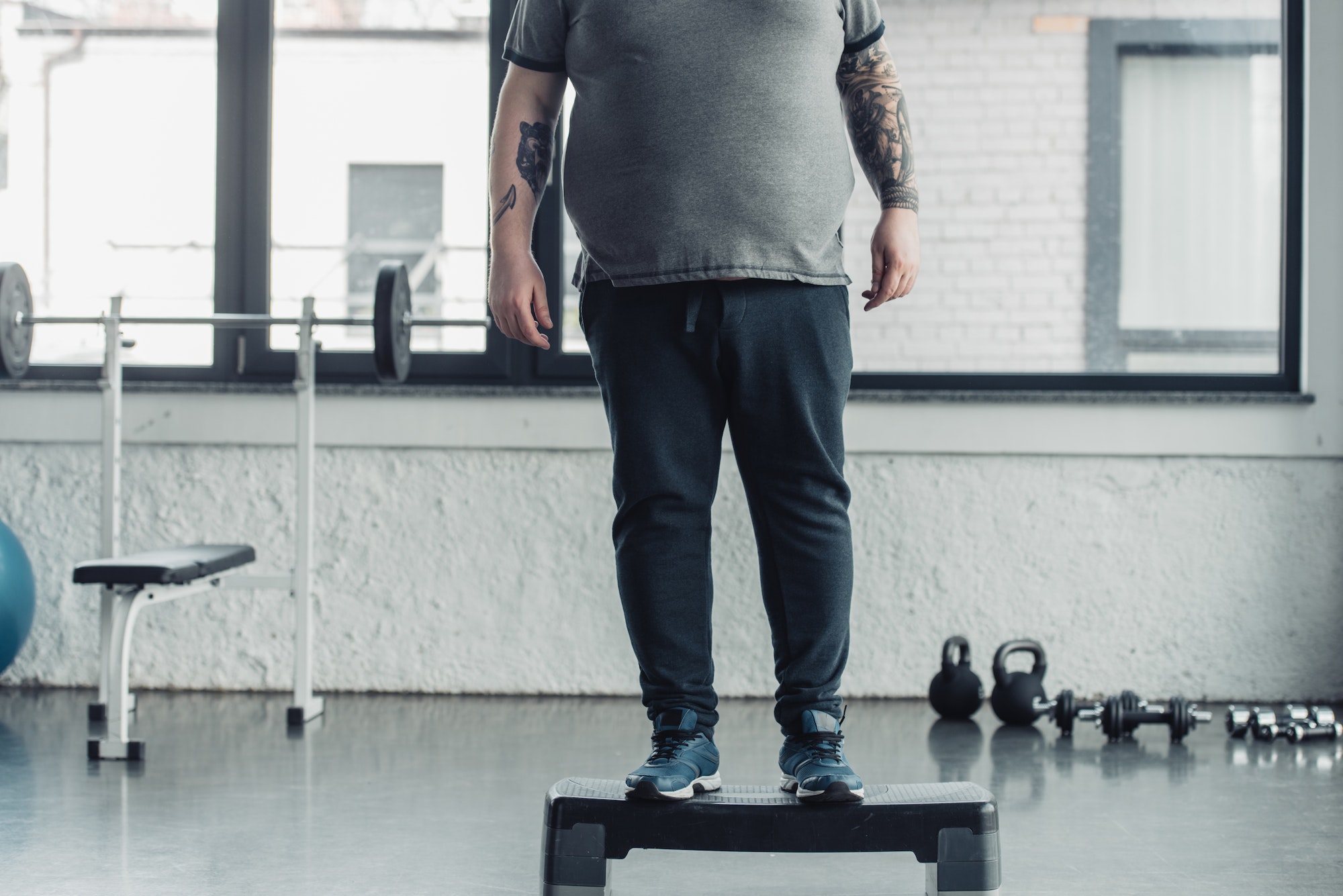 cropped view of overweight tattooed man standing on step platform at sports center